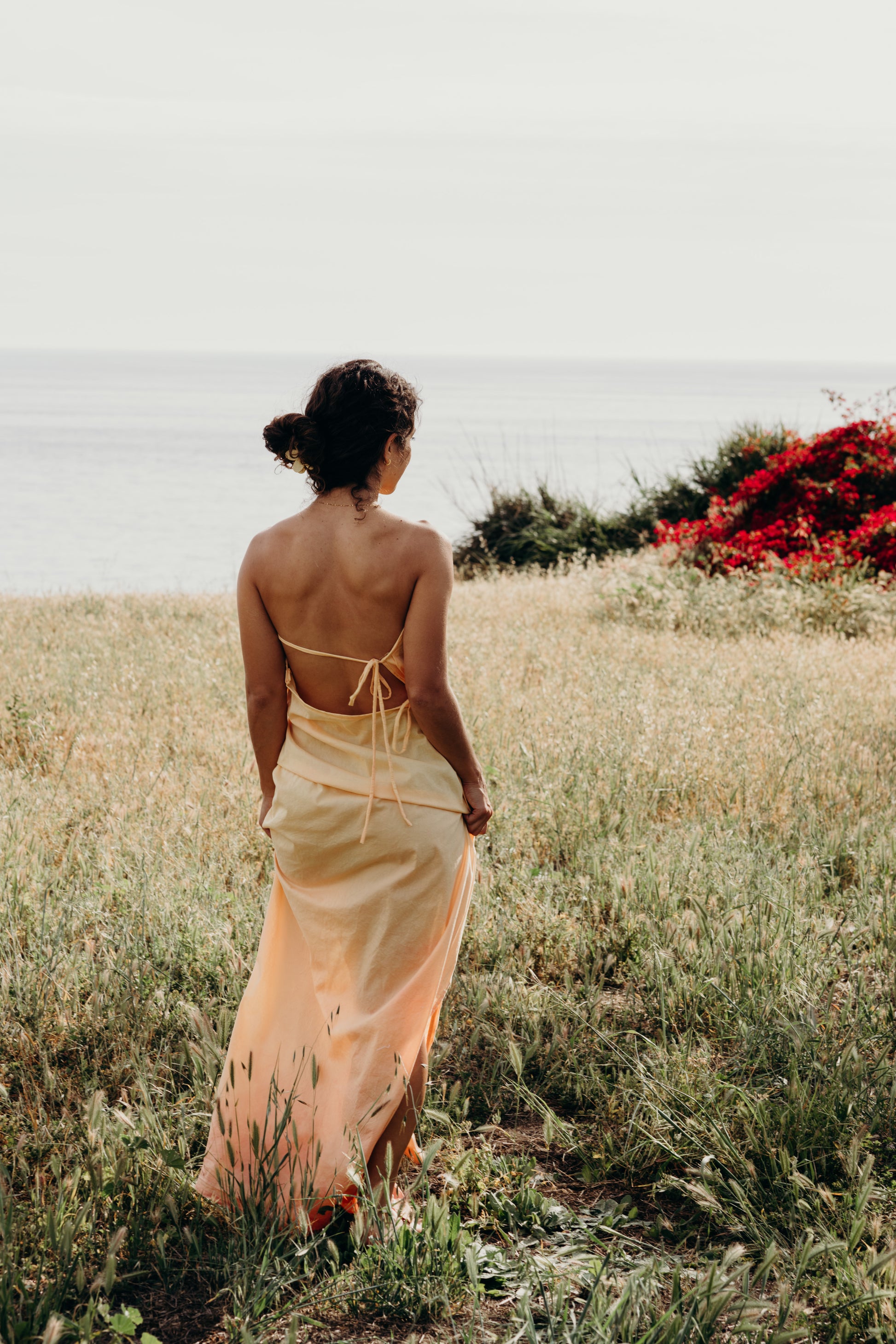 Woman in a yellow dress standing in a field with red flowers in the background