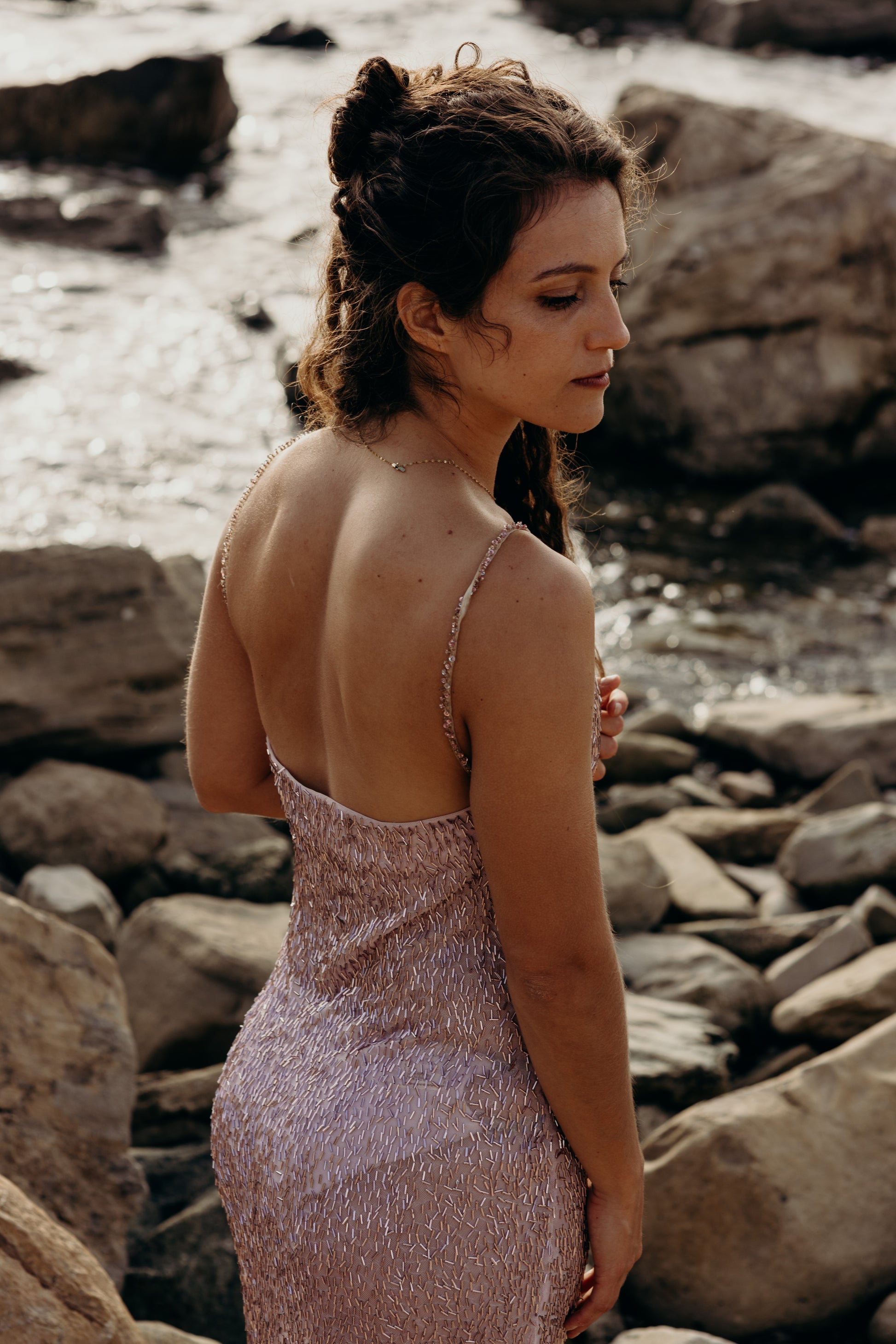 Woman in a pink dress standing on a rocky beach