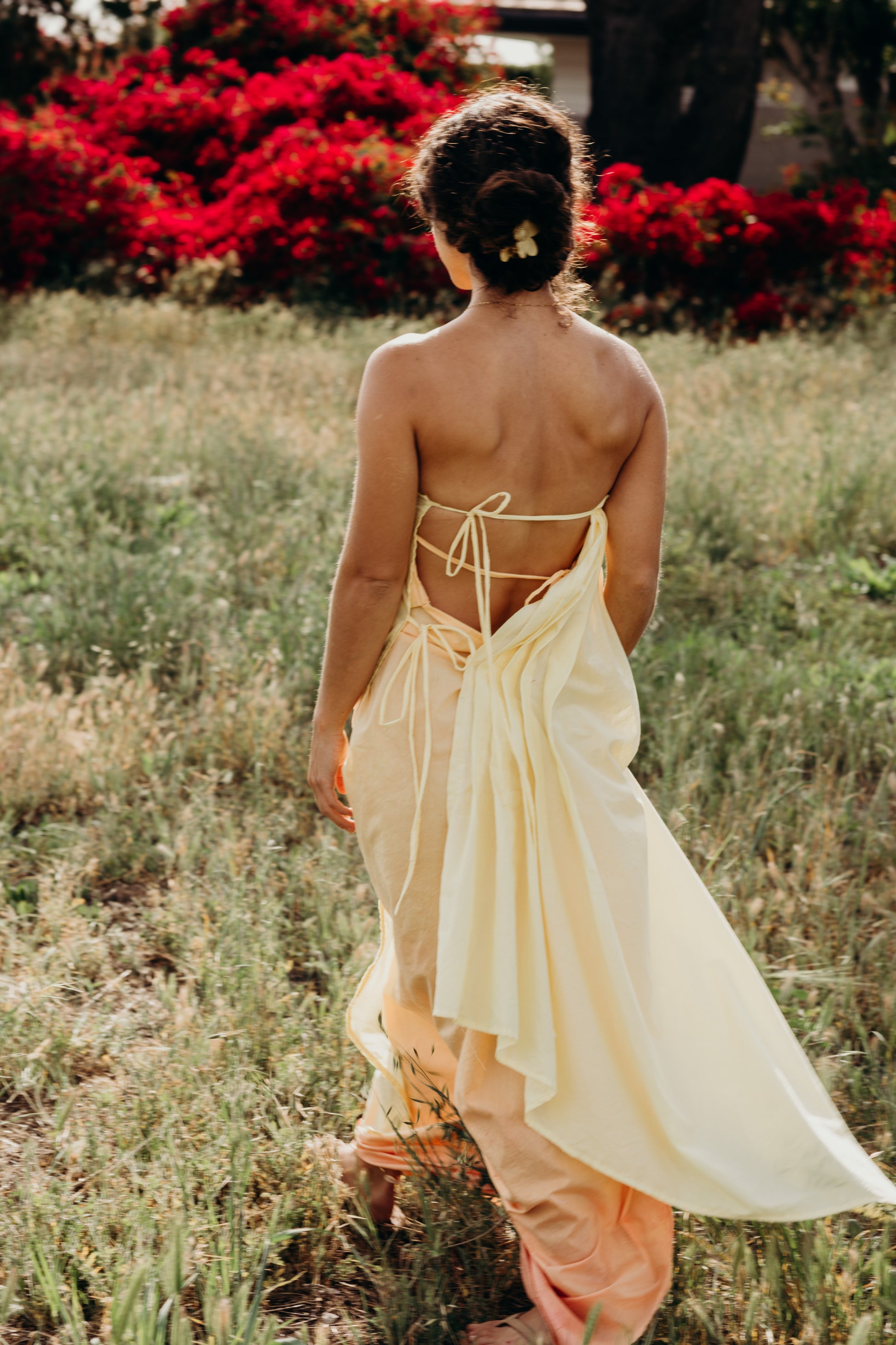 Woman in a flowing dress with an open back walking through a field with red flowers.