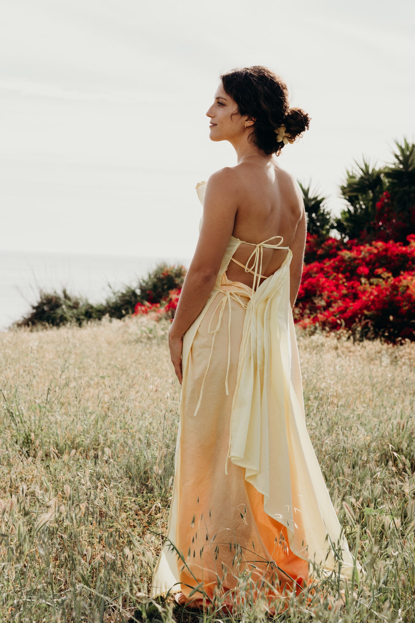 Woman in a flowing dress standing in a field with red flowers and greenery.