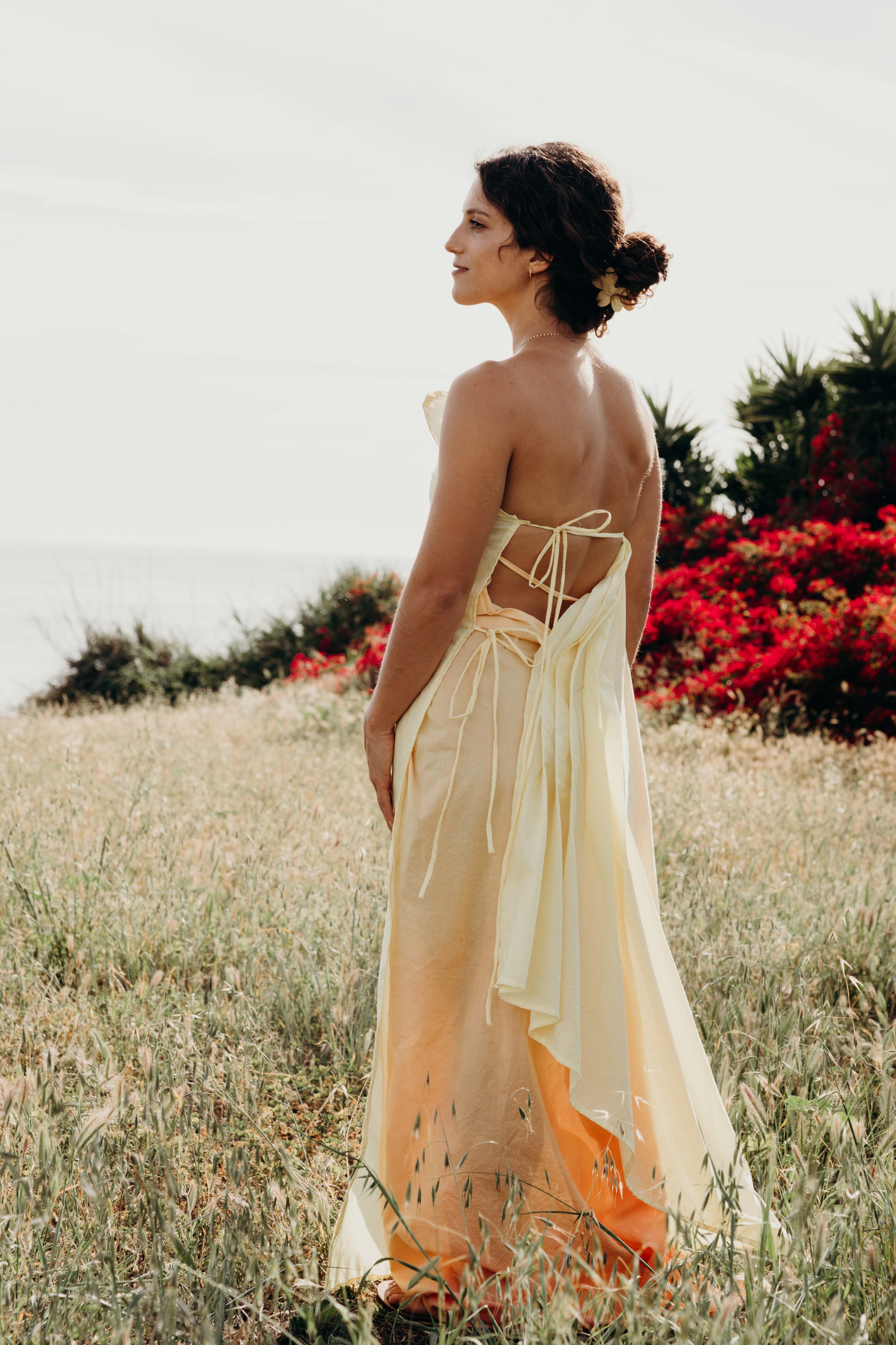 Woman in a flowing dress standing in a field with red flowers and greenery.