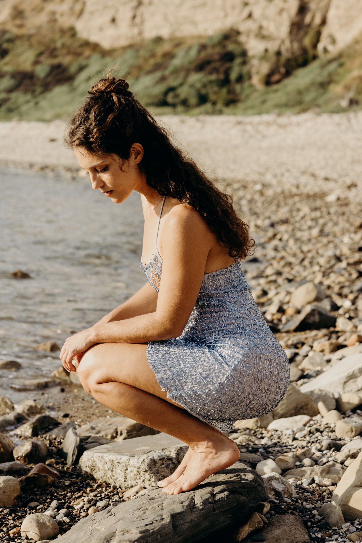 Woman squatting on a rocky beach with a scenic background