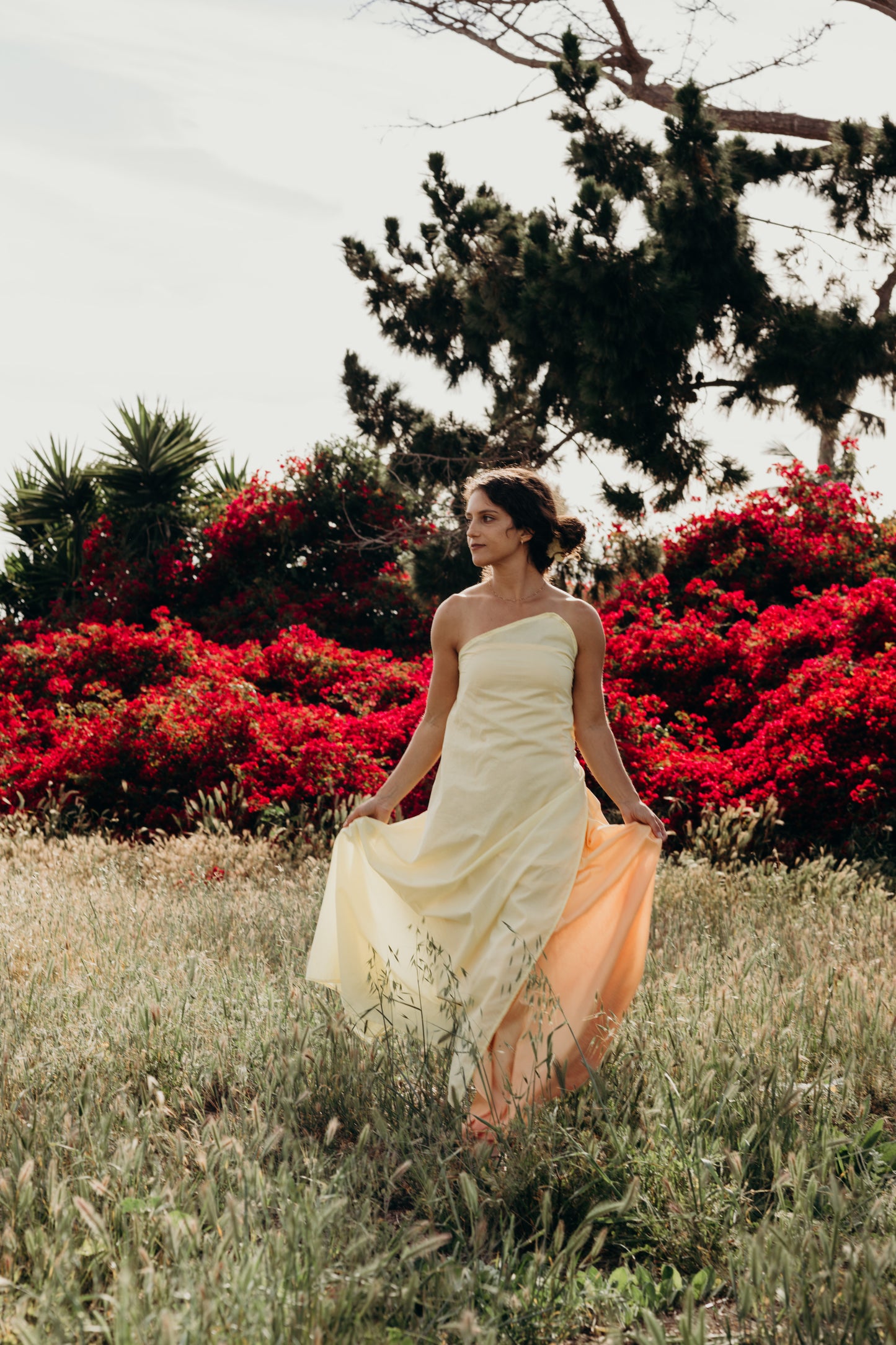 Woman in a white dress standing in a field with red flowers and trees in the background
