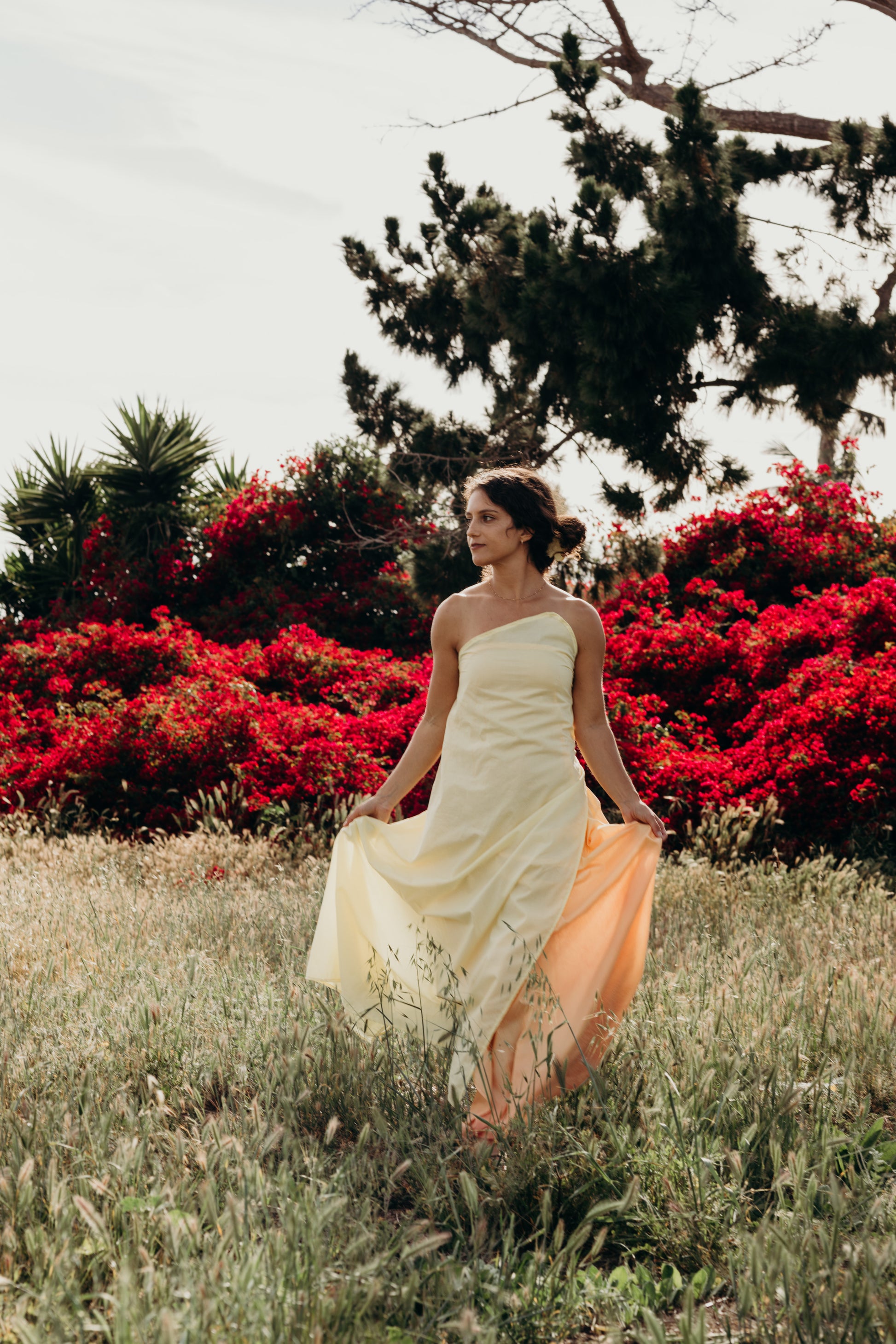 Woman in a white dress standing in a field with red flowers and trees in the background