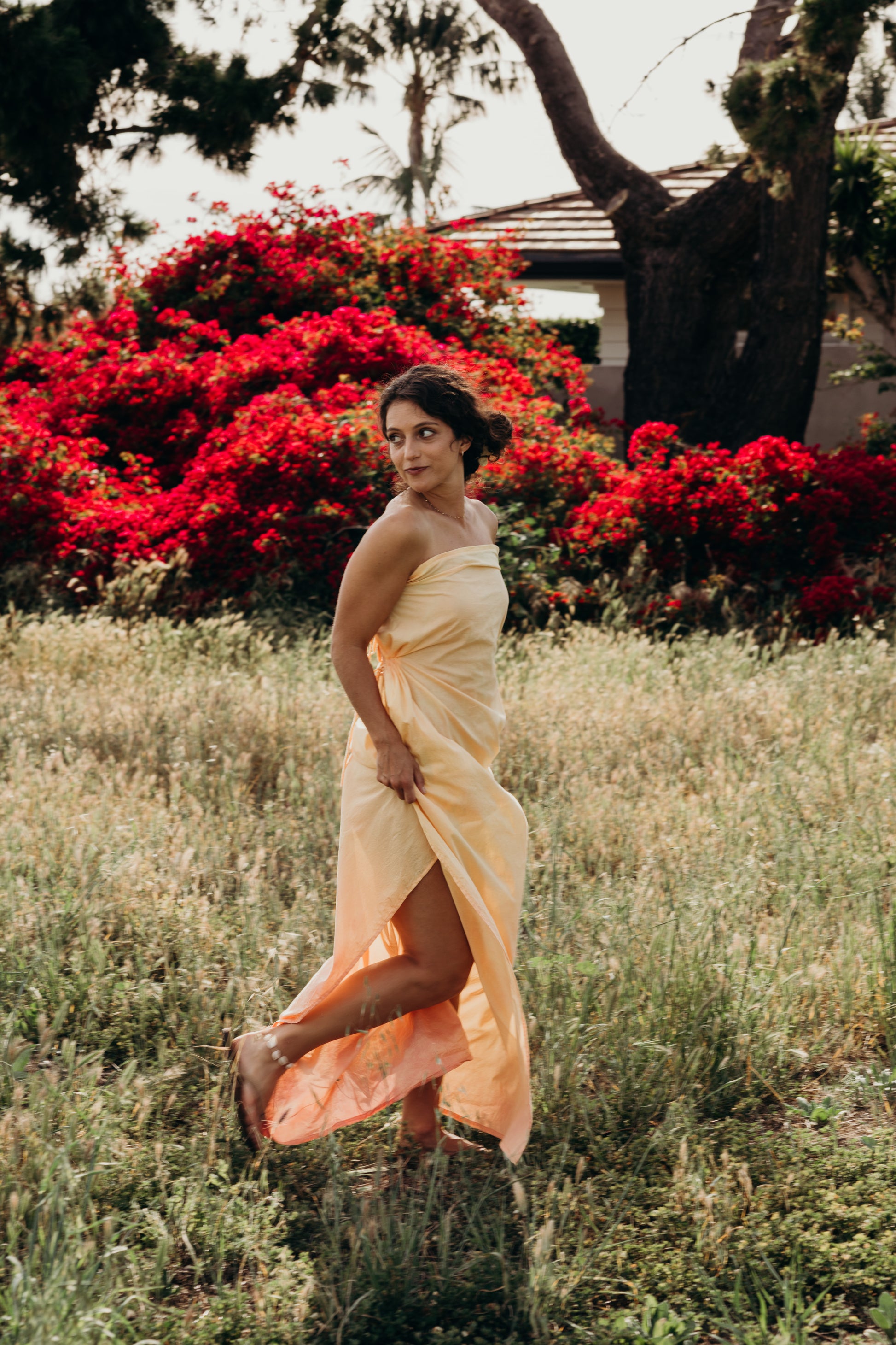 Woman in a yellow dress standing in a field with red flowers and trees in the background