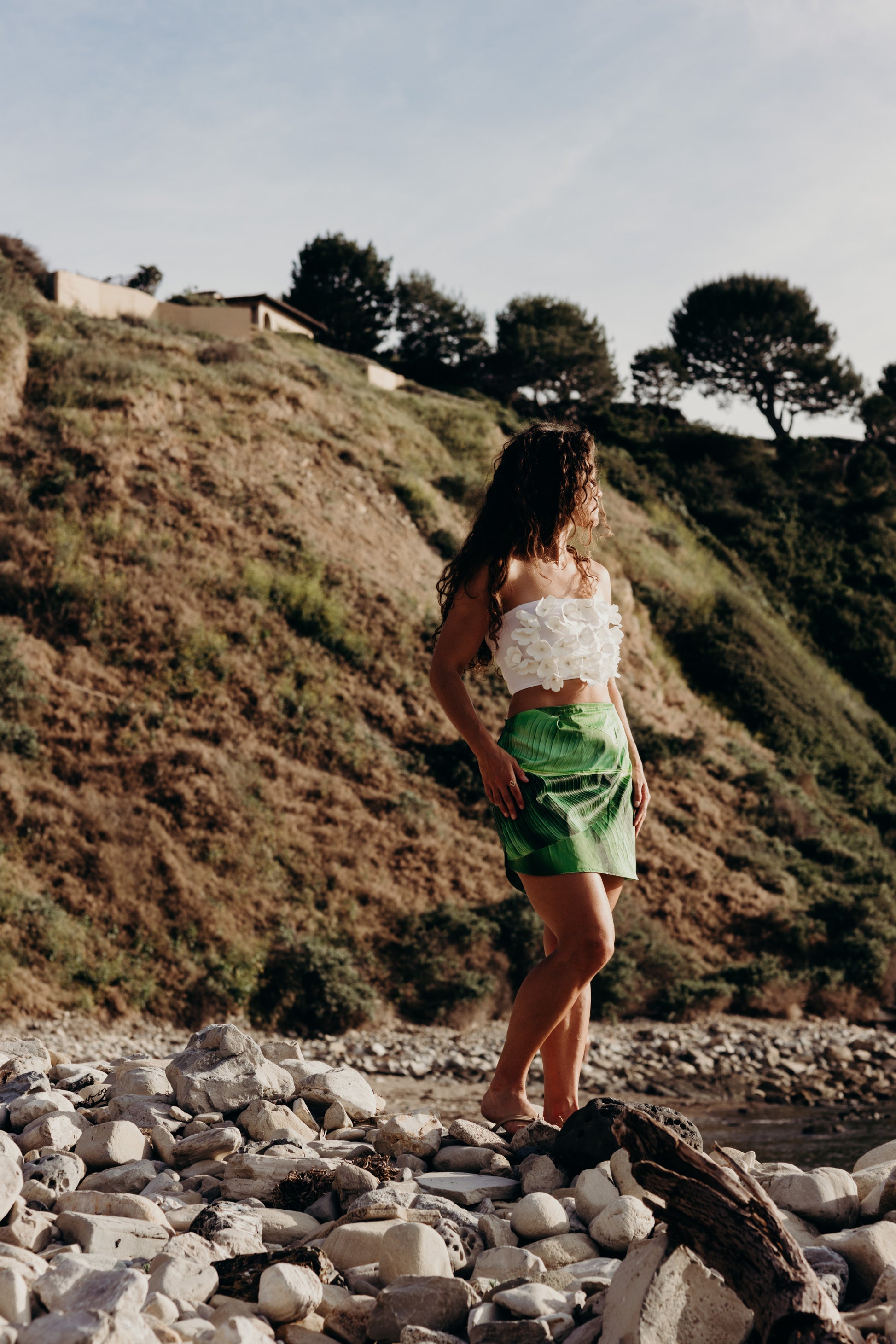 Woman standing on a rocky beach with a grassy hill in the background